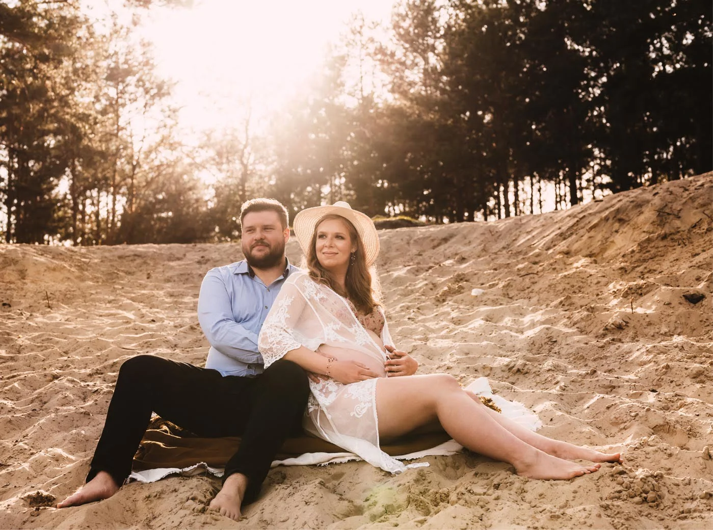kobieta w ciąży siedzi na plaży z mężem